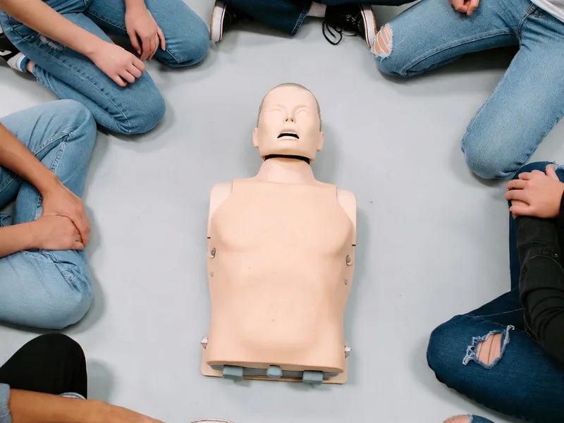Indoor CPR training session with learners seated in a circle around a practice manikin